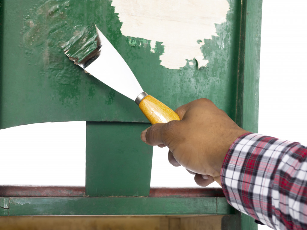 Close-up of man's hand peeling a green paint on the old chair